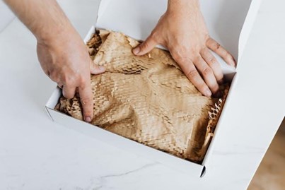 Close-up of hands preparing a box with packing material, ensuring valuables are secure for a move.