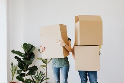 Two people carrying cardboard boxes in front of a white wall, ready for the new chapter post-packing for a move.