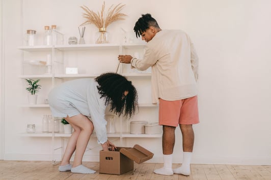 A couple organizing shelves and packing boxes in a bright room, symbolizing collaboration in packing and unpacking for a move.